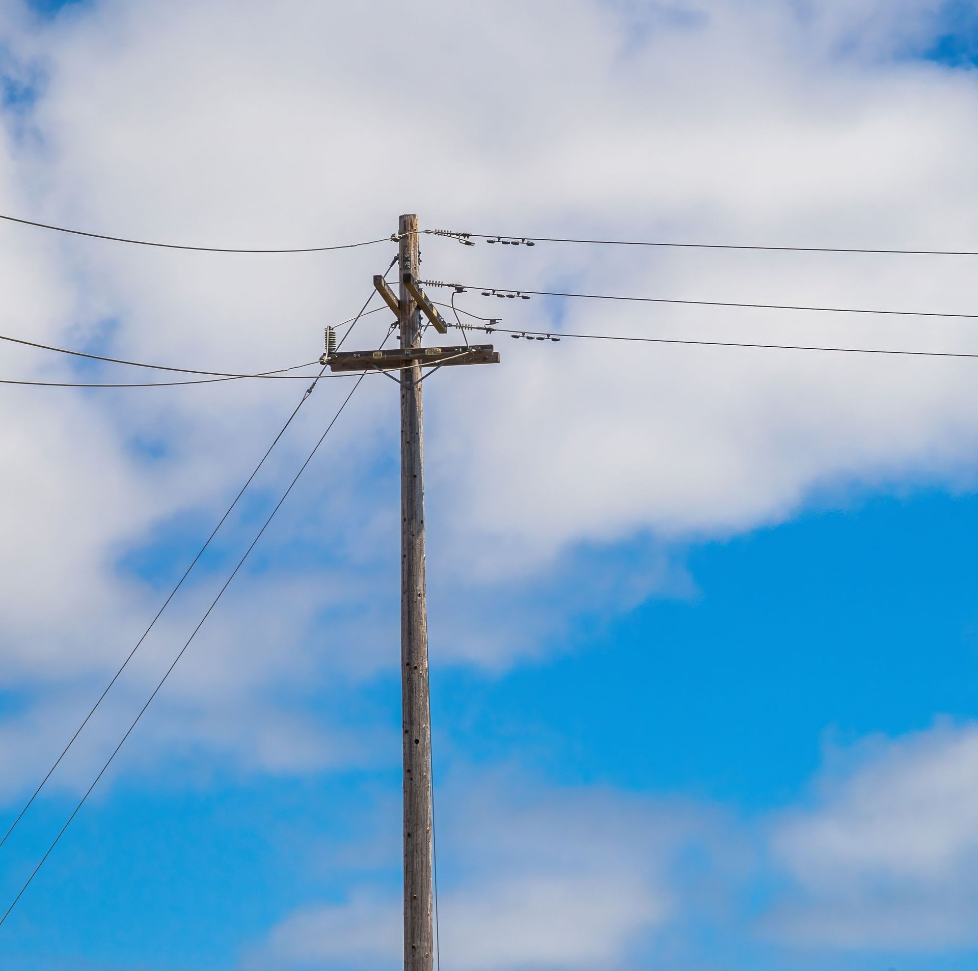 Utility pole with power lines against a blue sky and clouds