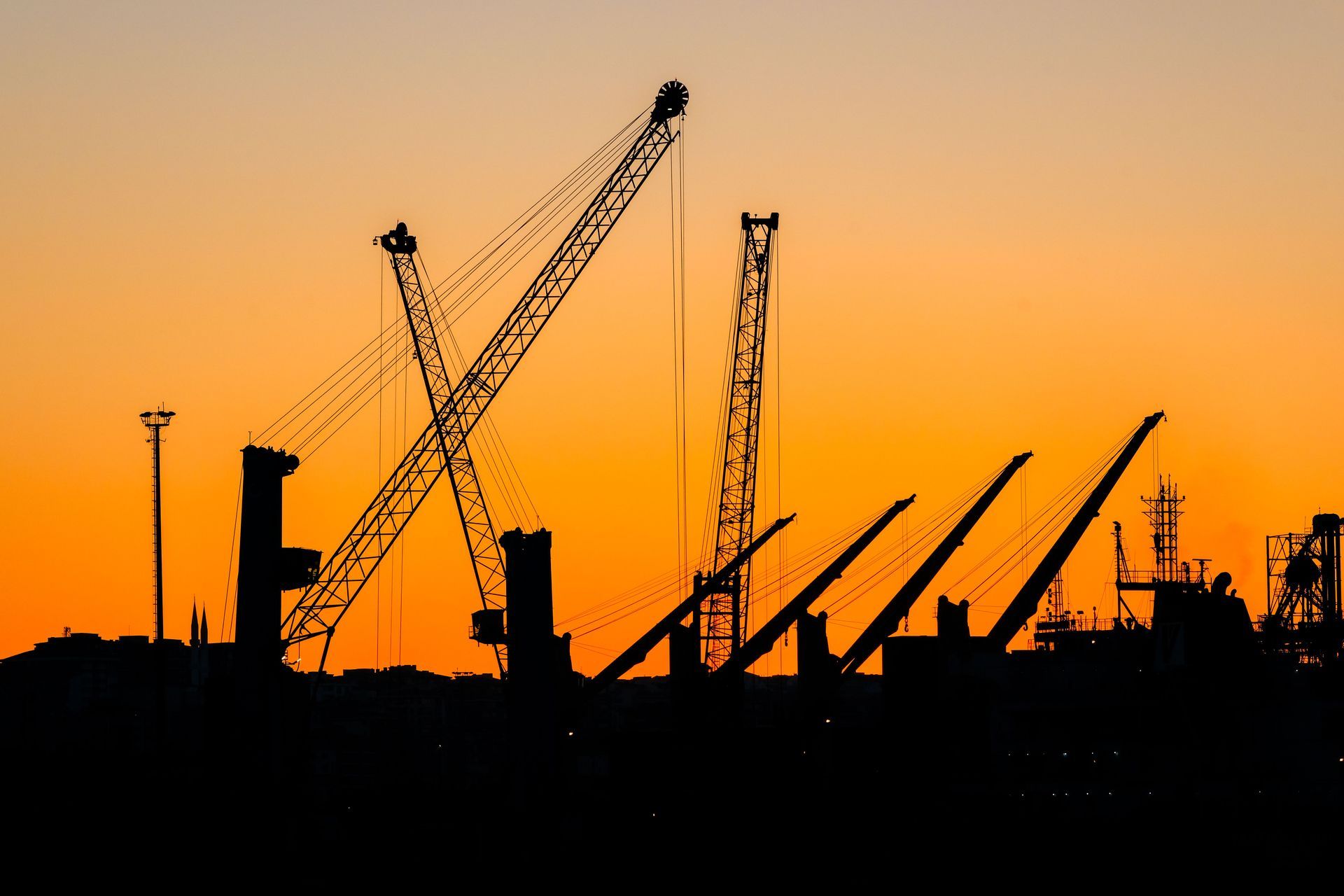 Silhouetted construction cranes against an orange sunset sky