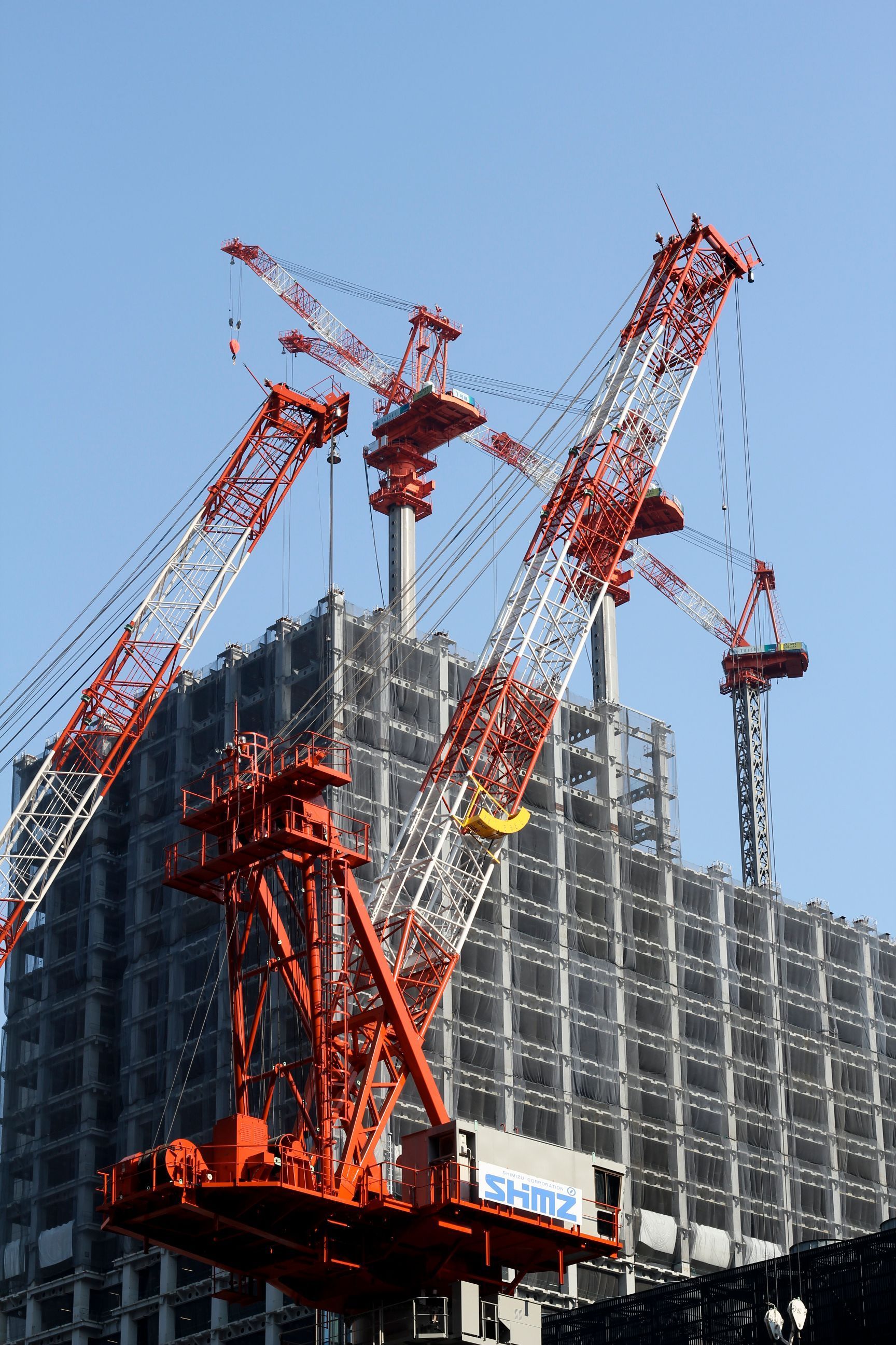 Crane assembly lifting a red-and-white construction crane beside a high-rise building under construction