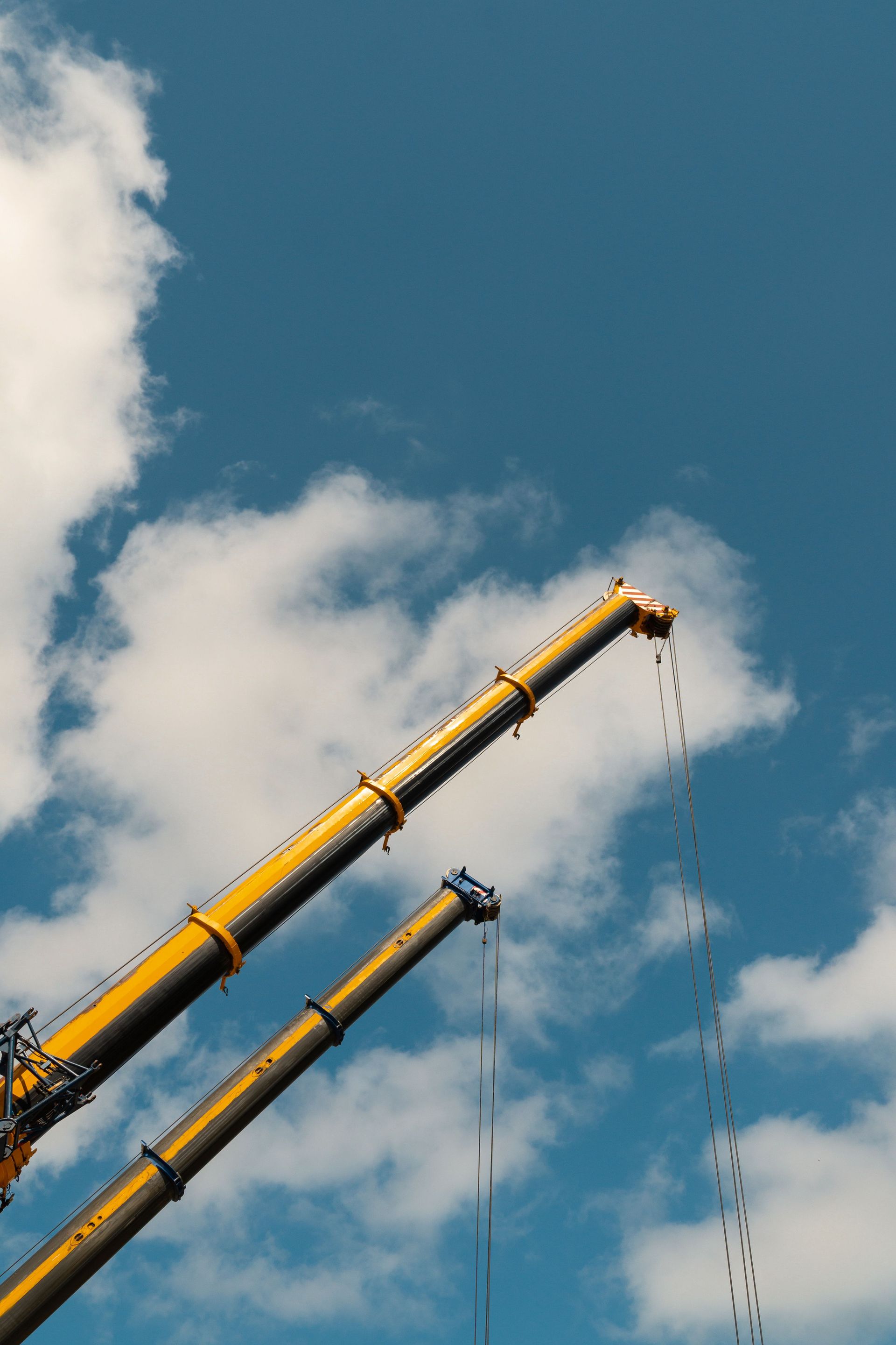 Yellow crane boom against blue sky with clouds, lifting cables hanging down