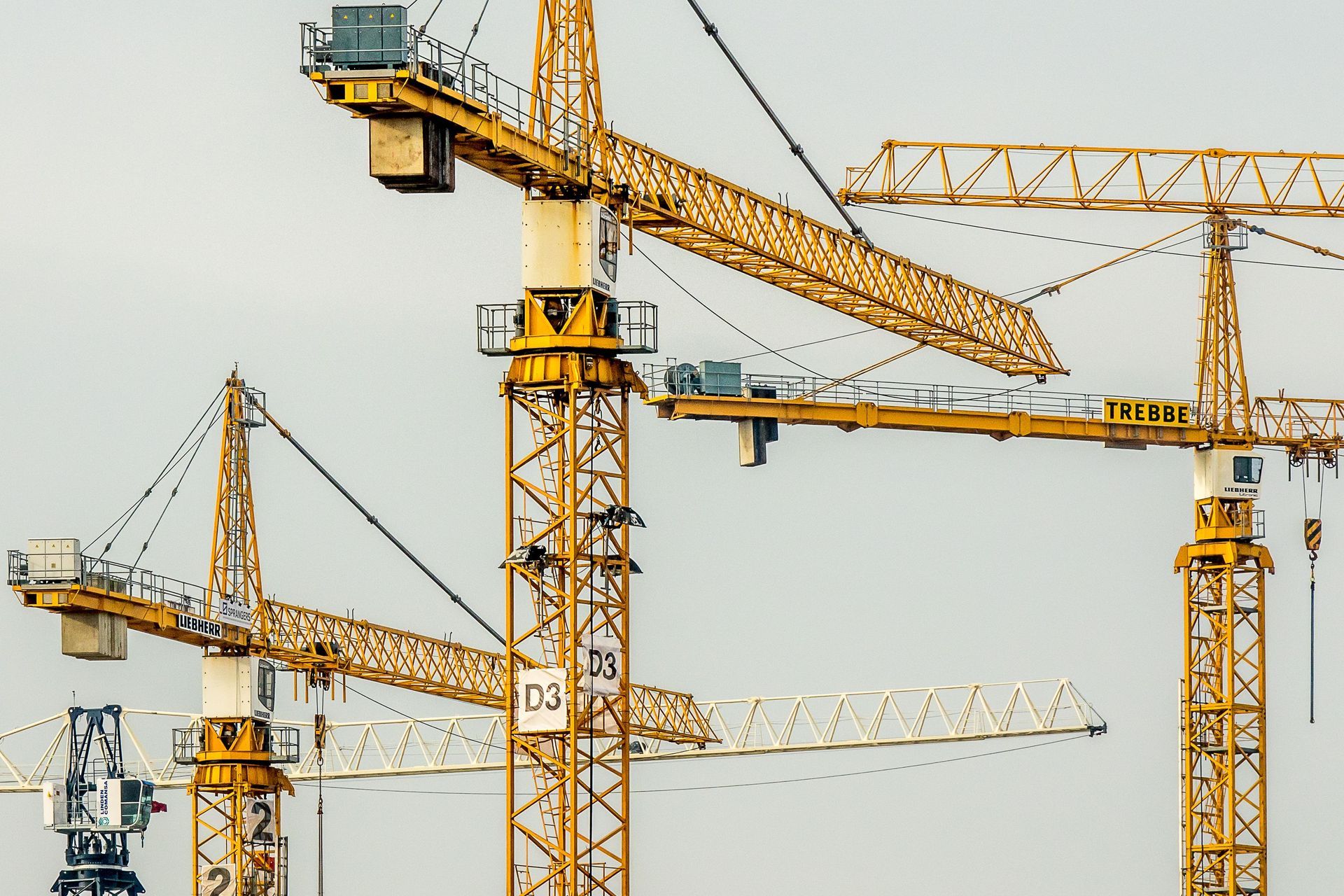Several yellow construction cranes against a pale sky at a building site