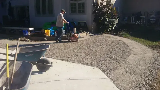 A man is pushing a wheelbarrow down a gravel driveway.