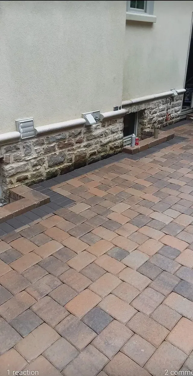A brick patio in front of a house with a stone wall.