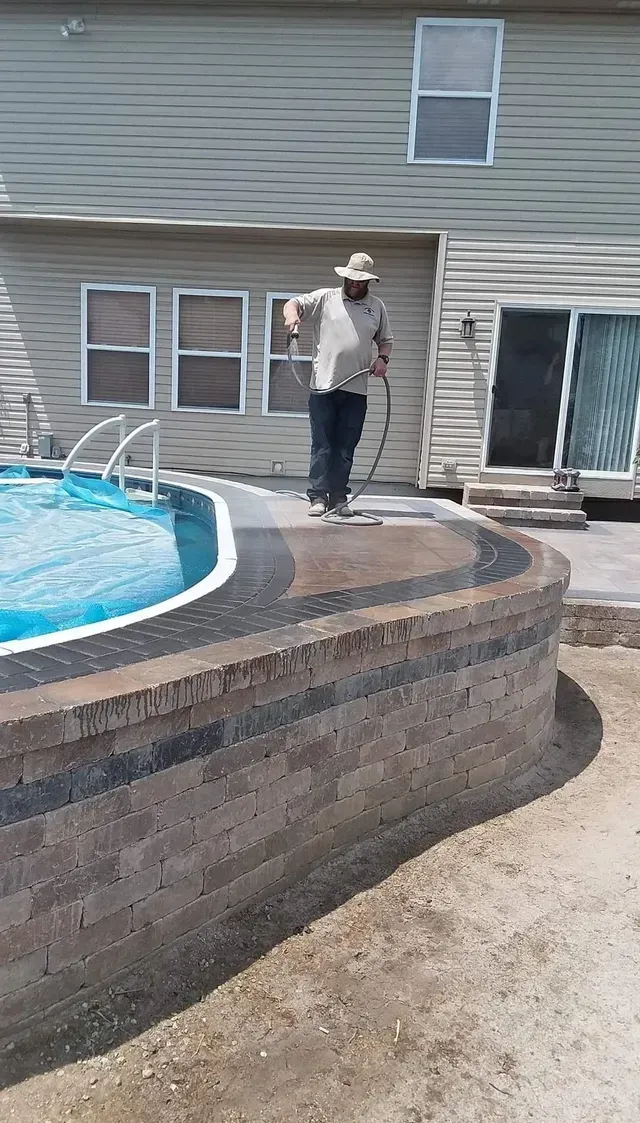 A man is standing next to a swimming pool in front of a house.
