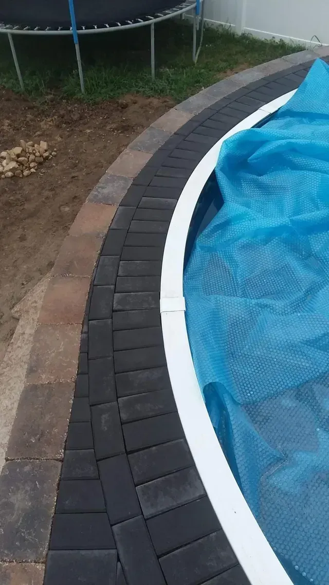 A trampoline is sitting next to a swimming pool covered in a blue tarp.