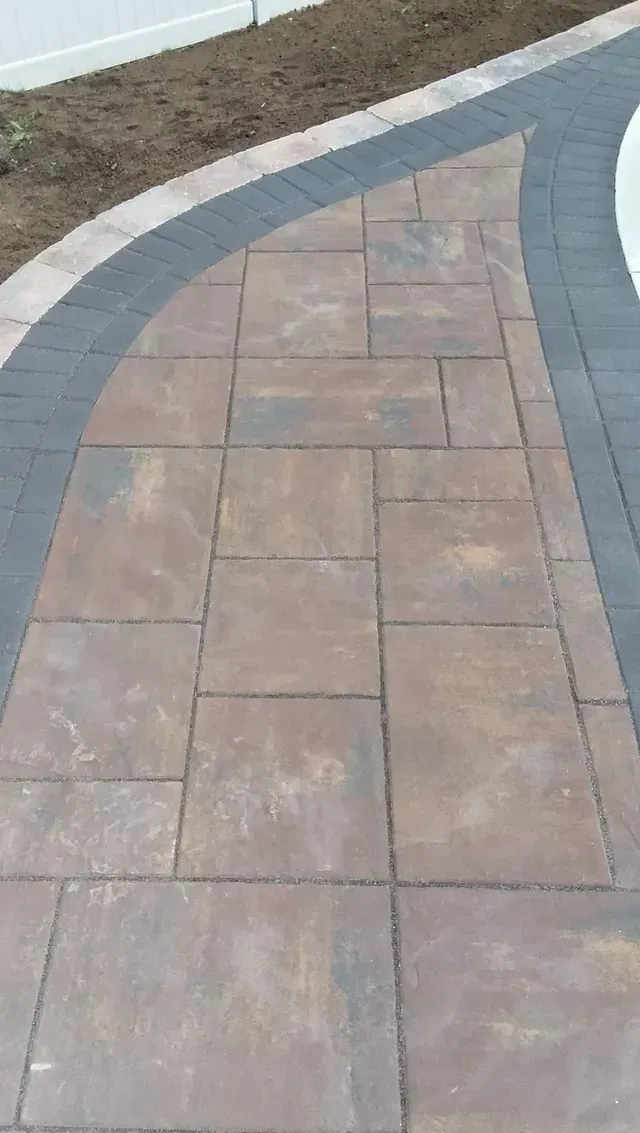 A close up of a brick walkway with a fence in the background.