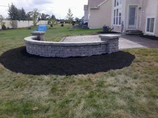 A brick wall is sitting in the middle of a lush green lawn in front of a house.