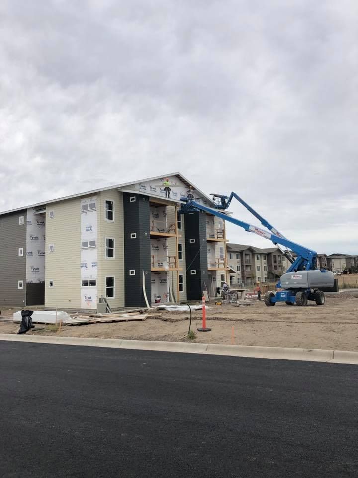Construction of an apartment building. A blue boom lift is used to work on the exterior under a cloudy sky.