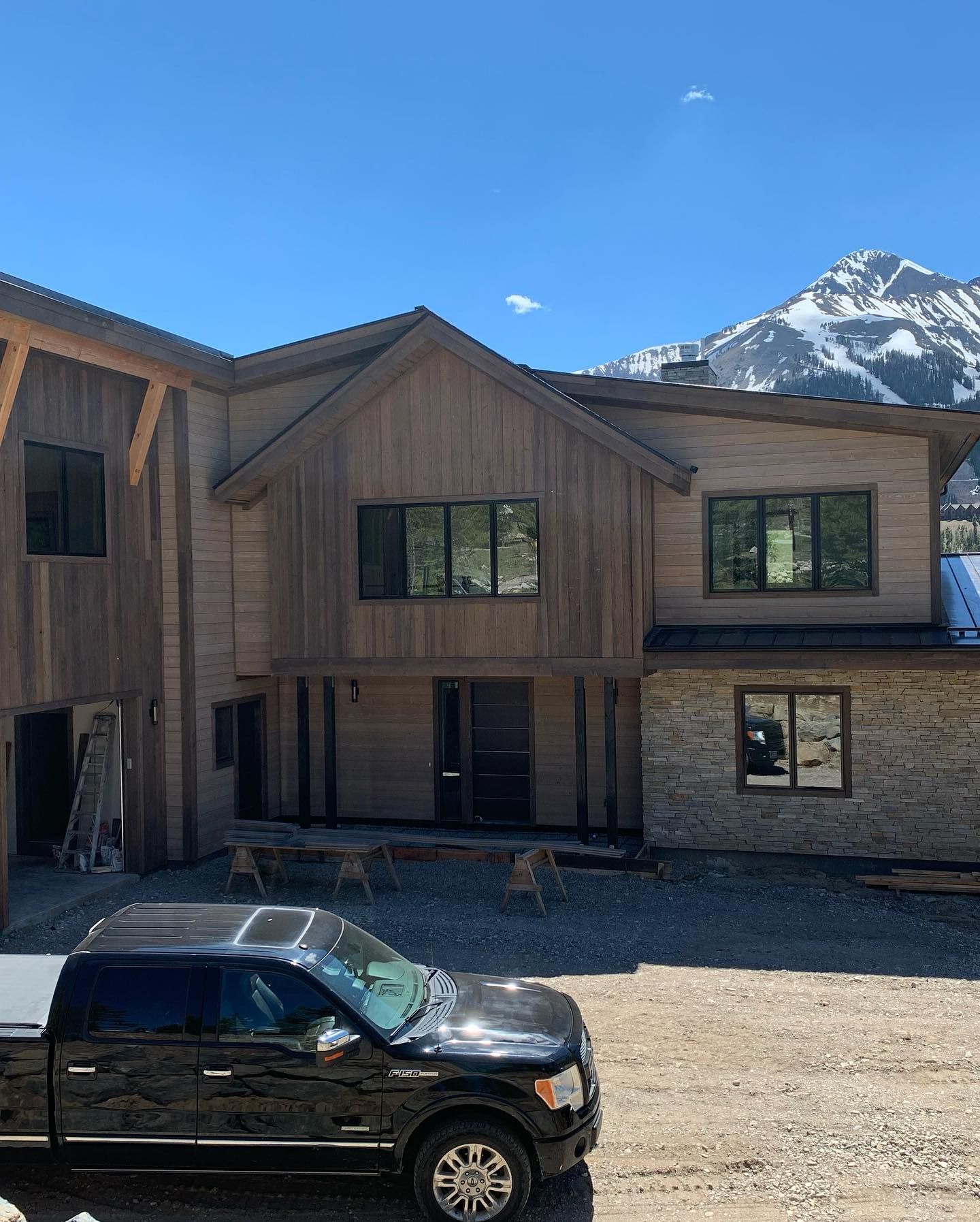 Two-story house with wood siding, windows, and a truck parked out front, with a mountain in the background.