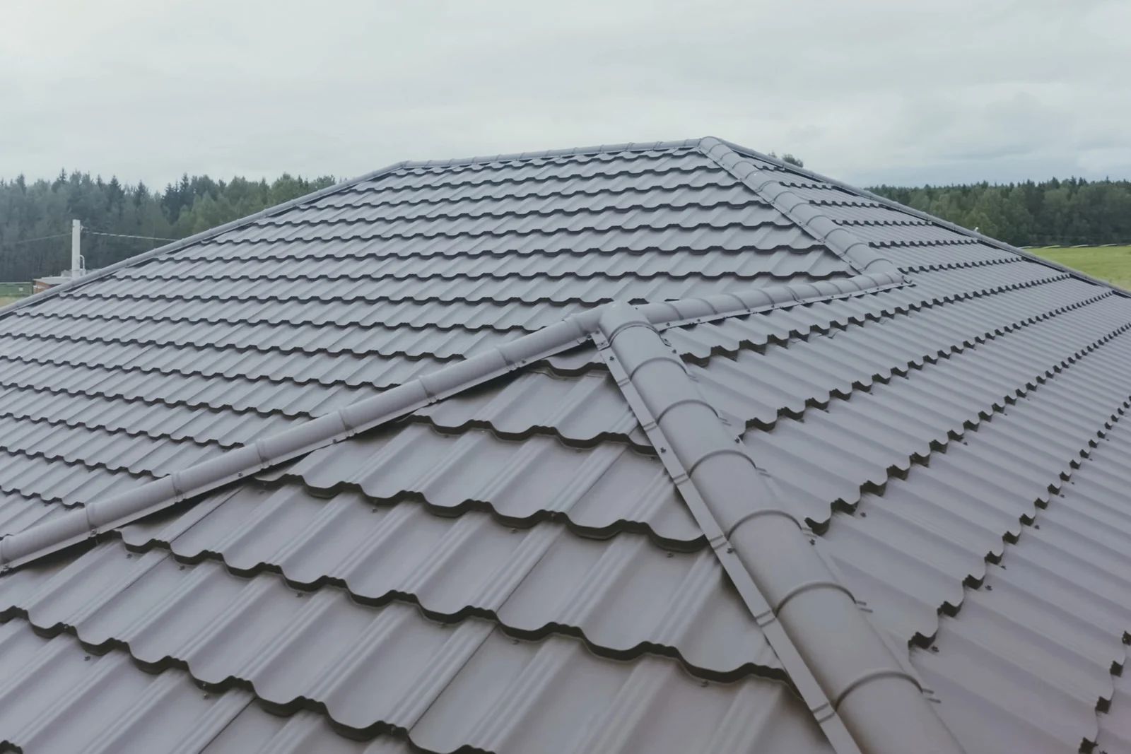 Gray metal-tiled roof with intersecting ridges against a cloudy sky