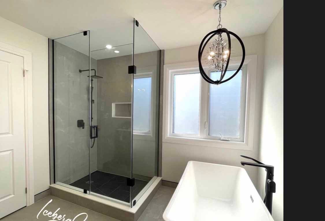 Modern bathroom with glass shower, freestanding tub, double windows, and a black pendant light.