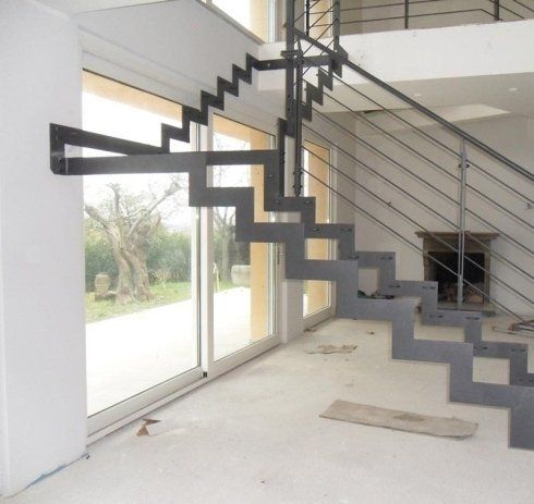 Moderna scala in acciaio fissata a una parete bianca e a una grande finestra.