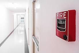 Red fire alarm box on a white hallway wall with a long corridor in the background