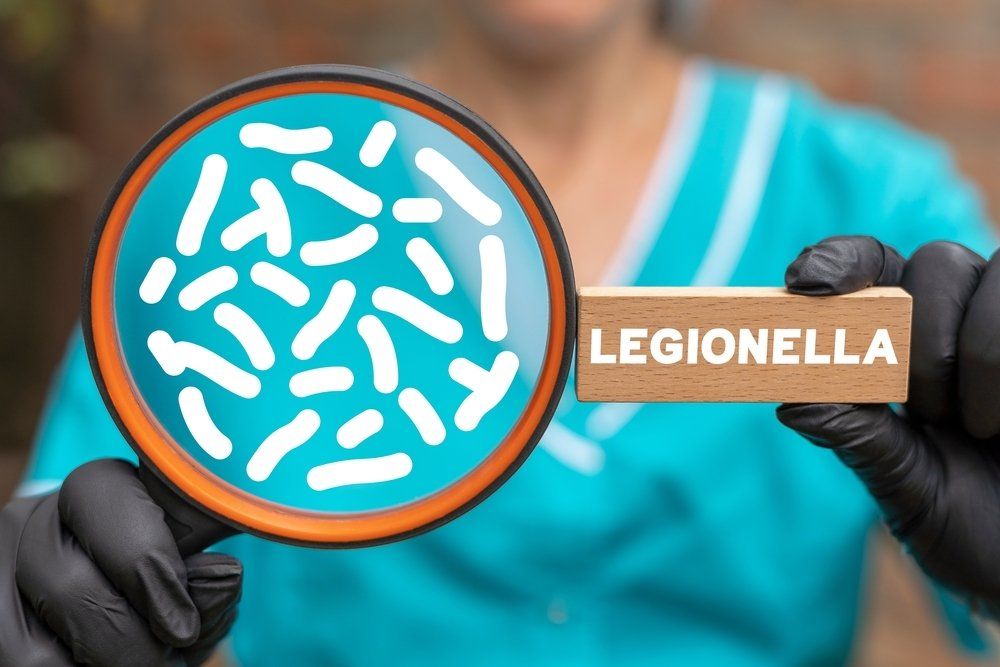A person is holding a magnifying glass and a wooden sign that says legionella.
