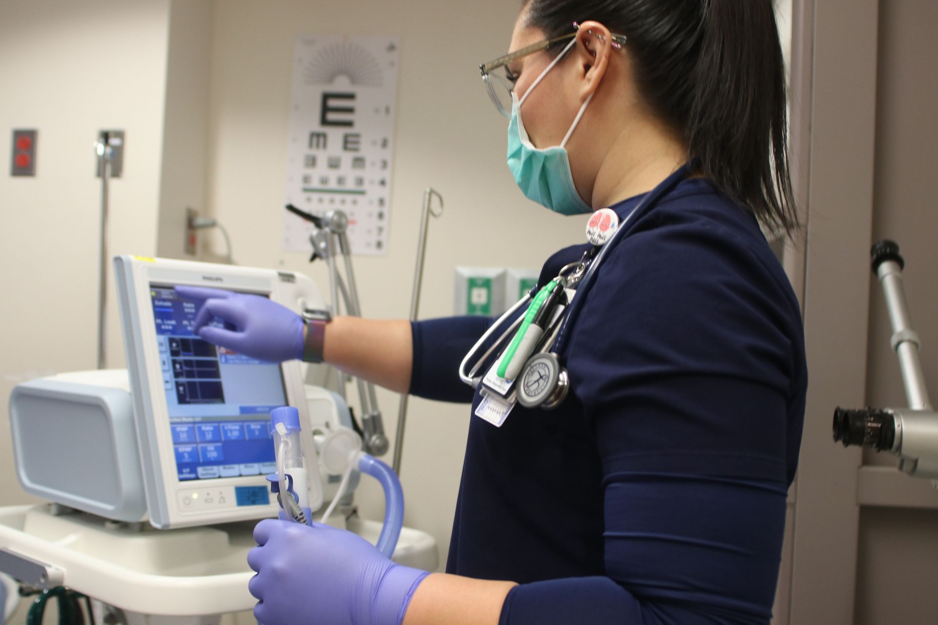 A nurse wearing a mask and gloves is working on a machine.