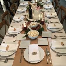 A long table set for a dinner party with plates , napkins , silverware and a bottle of wine.