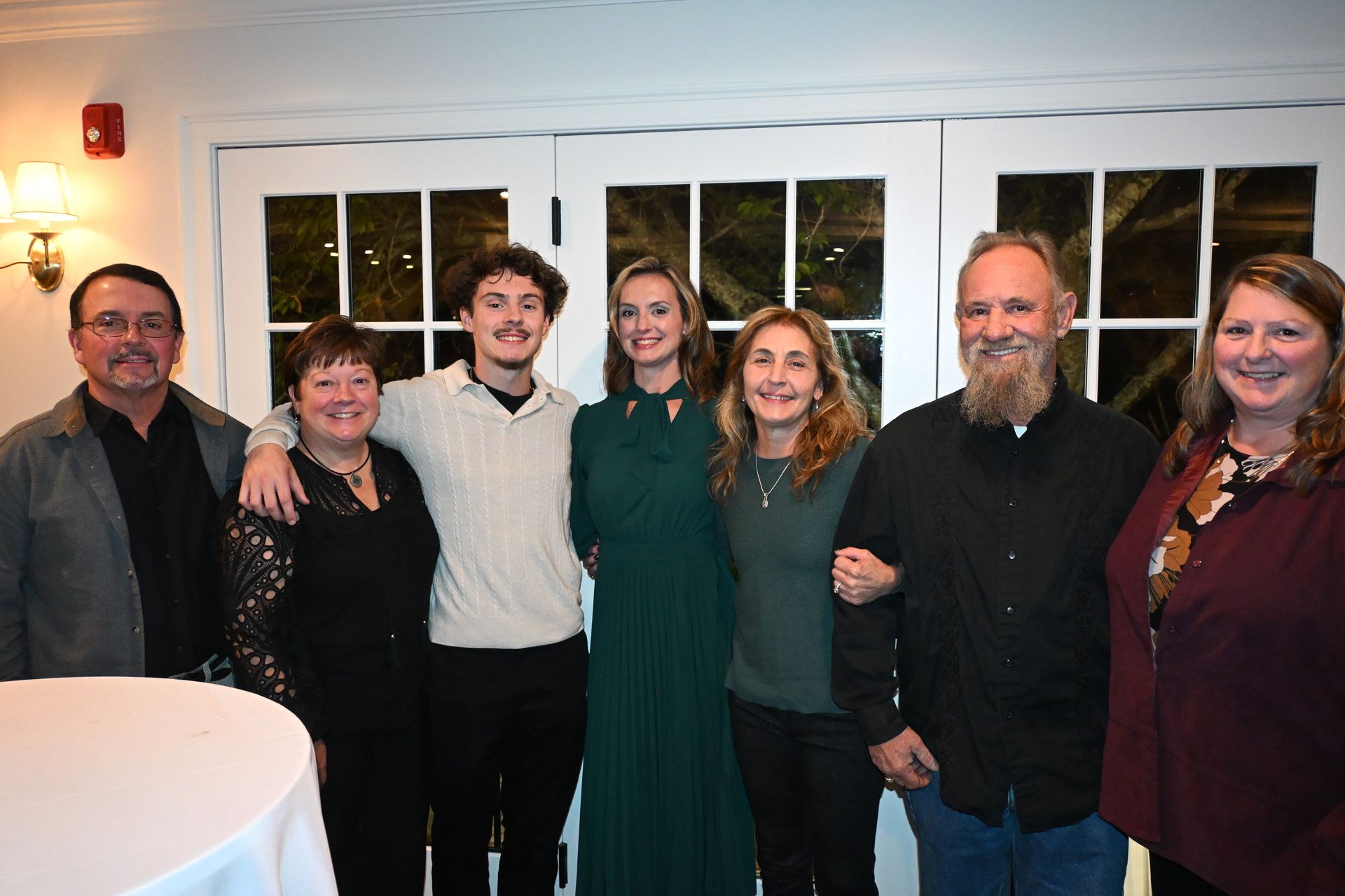 Six people posing together indoors in front of windows, smiling at the camera.
