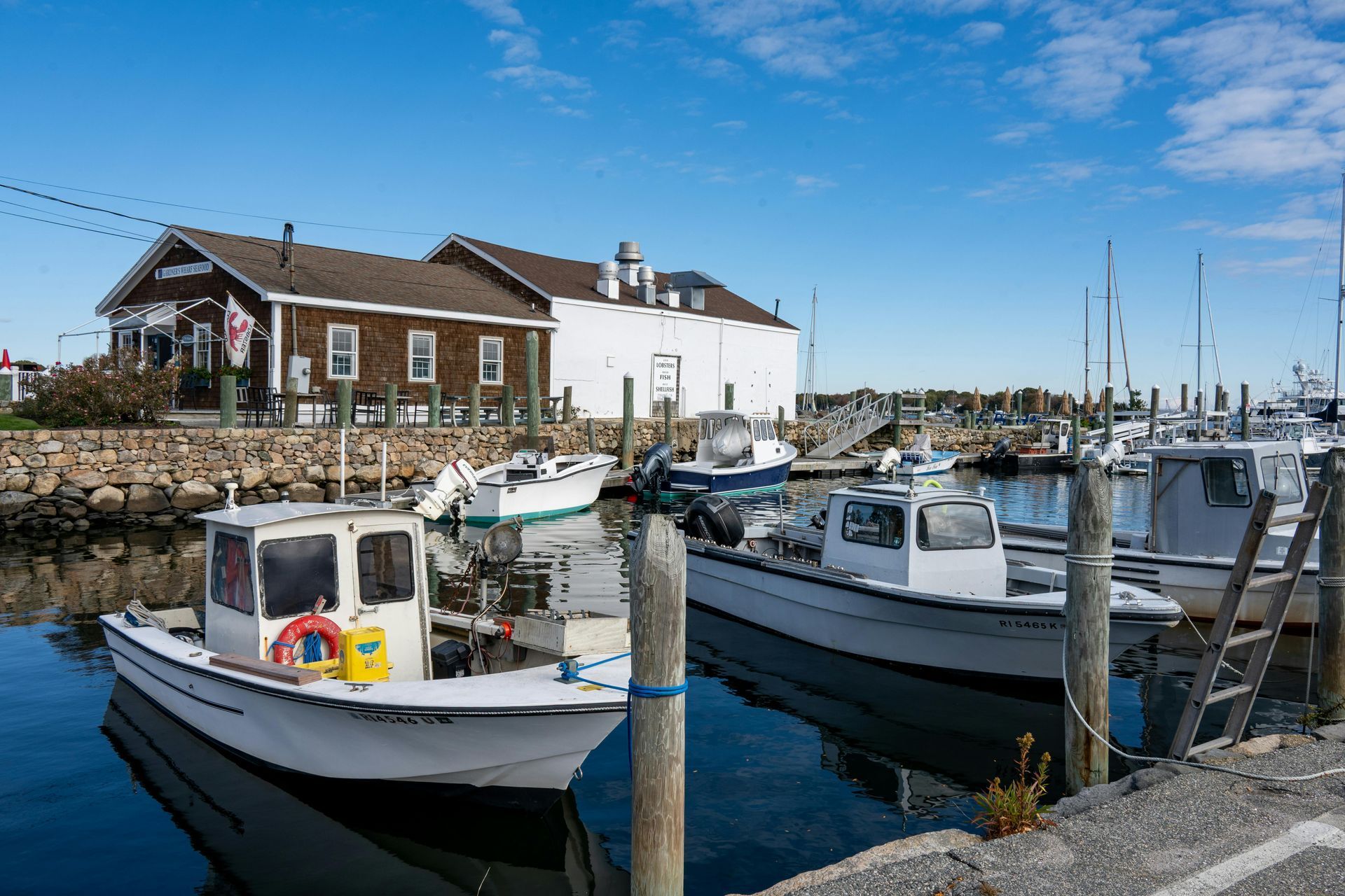 Small fishing boats docked in a harbor beside a stone wall and waterfront buildings under a clear blue sky