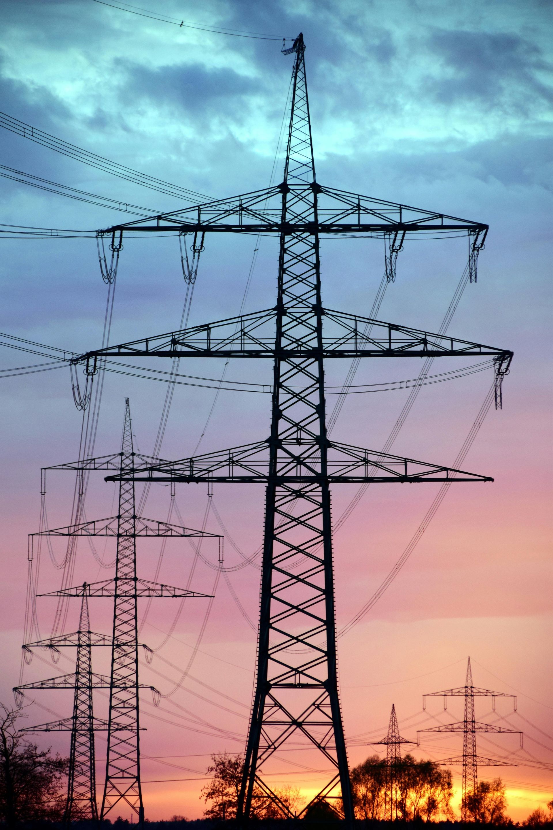 High-voltage power transmission towers silhouetted against a pink and blue sunset sky
