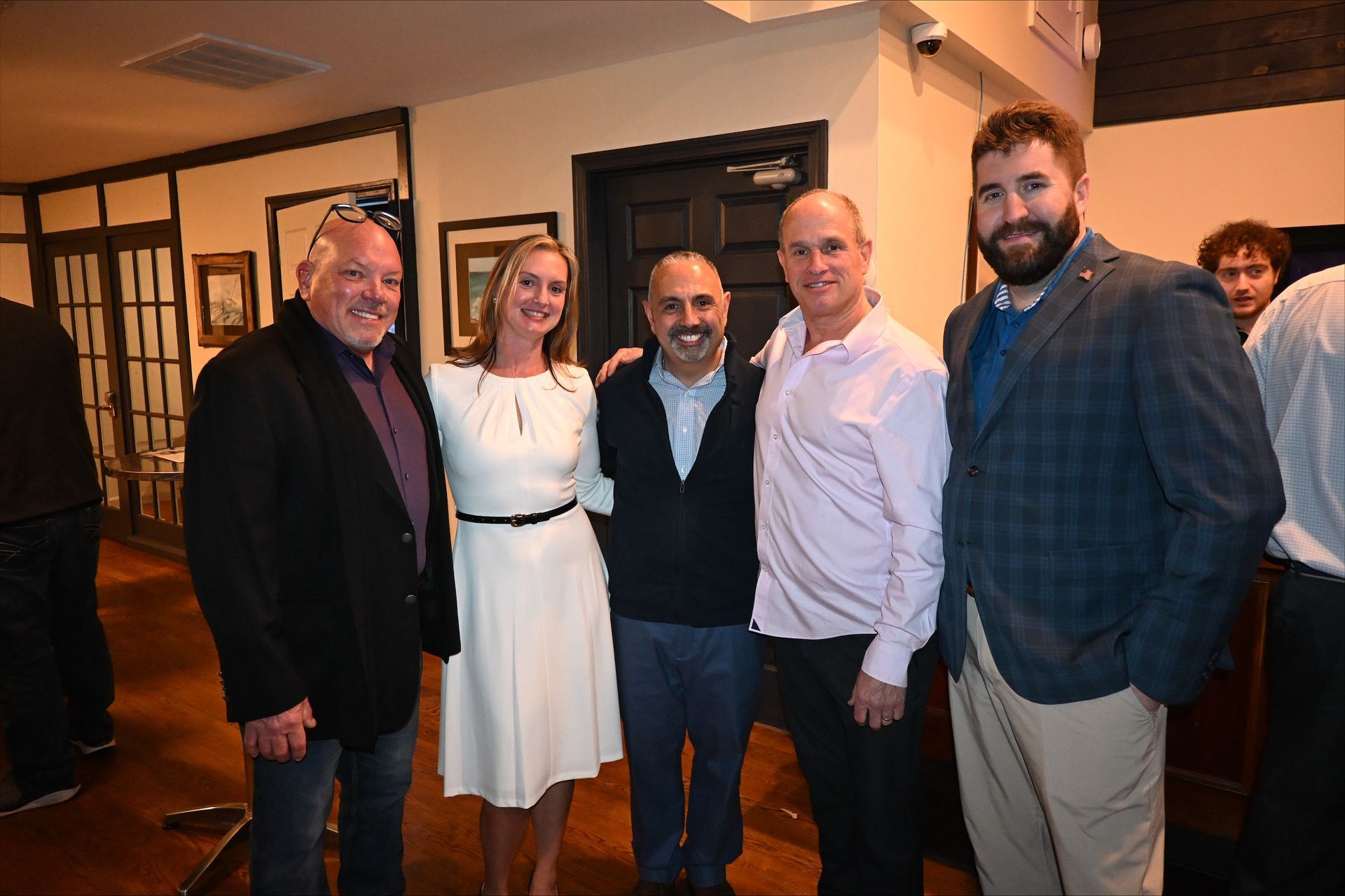 Five people posing together indoors at a social event, smiling in semi-formal attire.