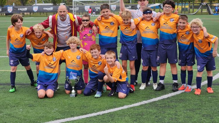 Youth soccer team in orange jerseys posing on a field with a coach in the center