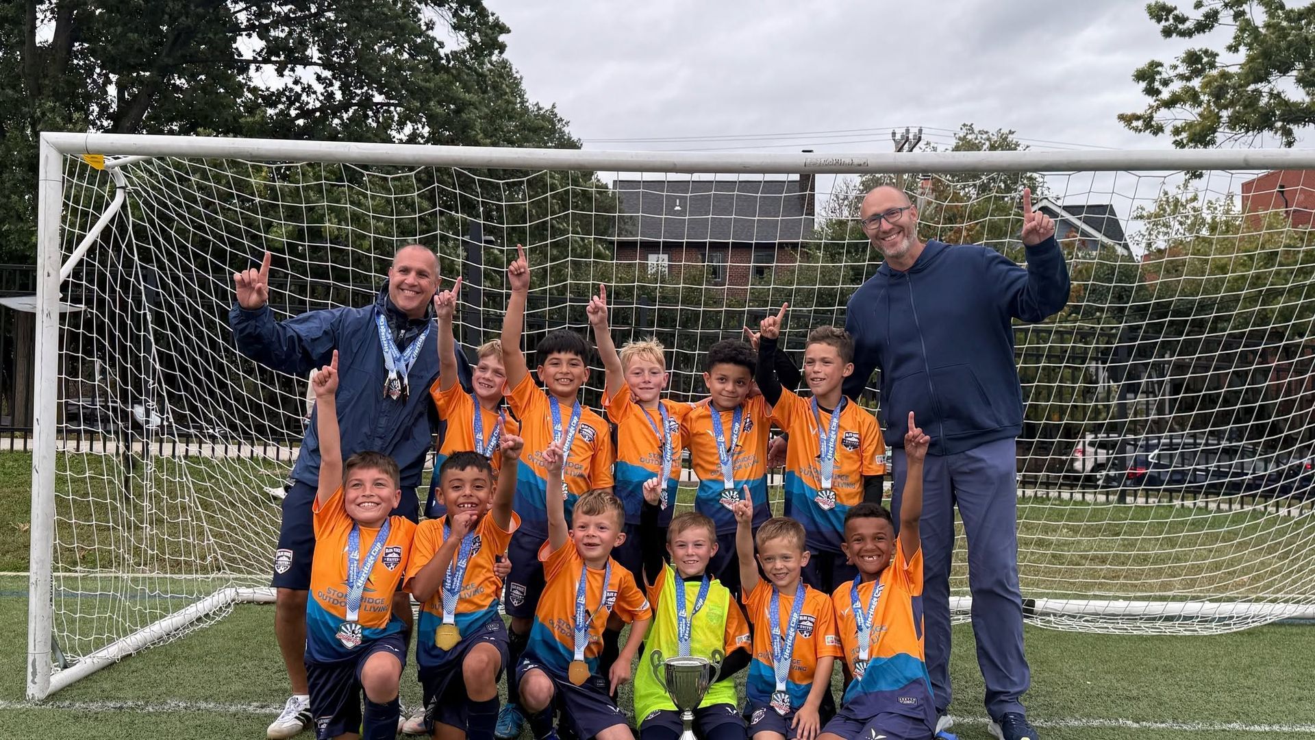 Youth soccer team in orange uniforms posing on a field in front of a goal and net