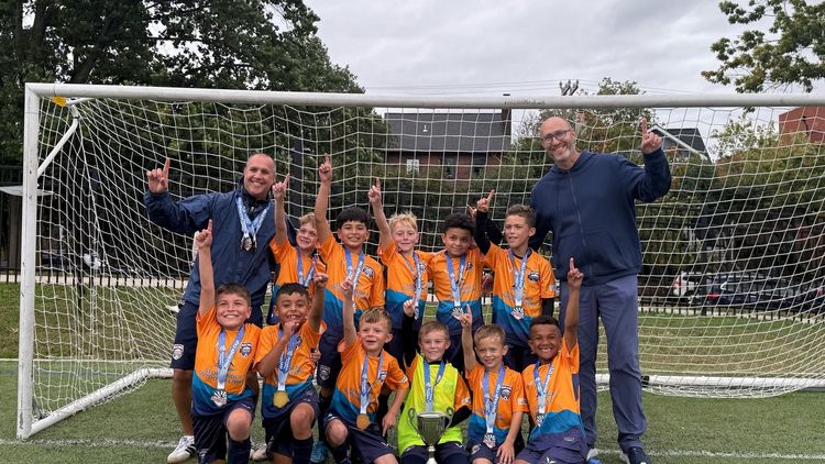 Youth soccer team in orange uniforms posing on a field in front of a goal and net