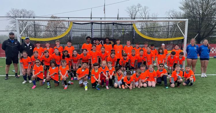 Youth soccer team in orange uniforms posing on a field in front of a goal and net