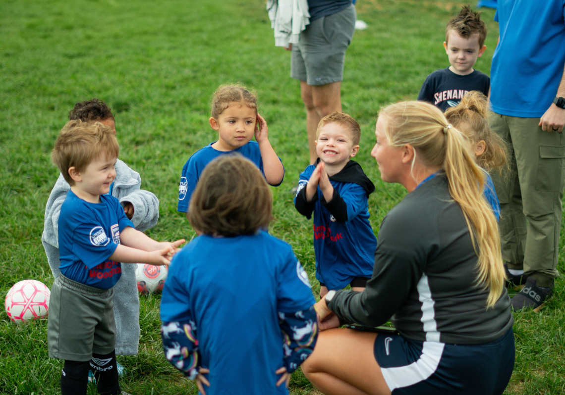 Two children playing soccer on a grassy field, one in navy and red, the other in white and blue