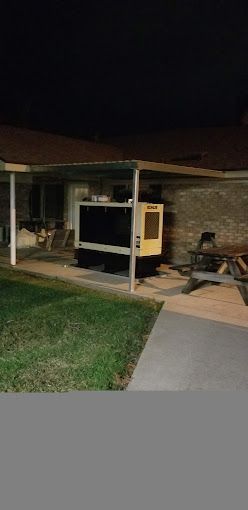 A large generator is sitting under a canopy in front of a house at night.