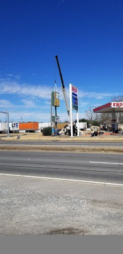 A crane is lifting a sign in front of a gas station.