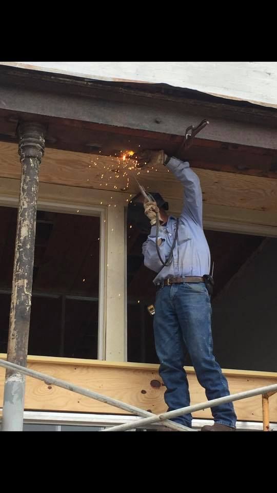 A man is welding a piece of wood on a porch.