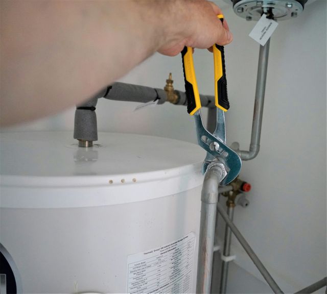 Hand using pliers on a pipe near a white water heater.