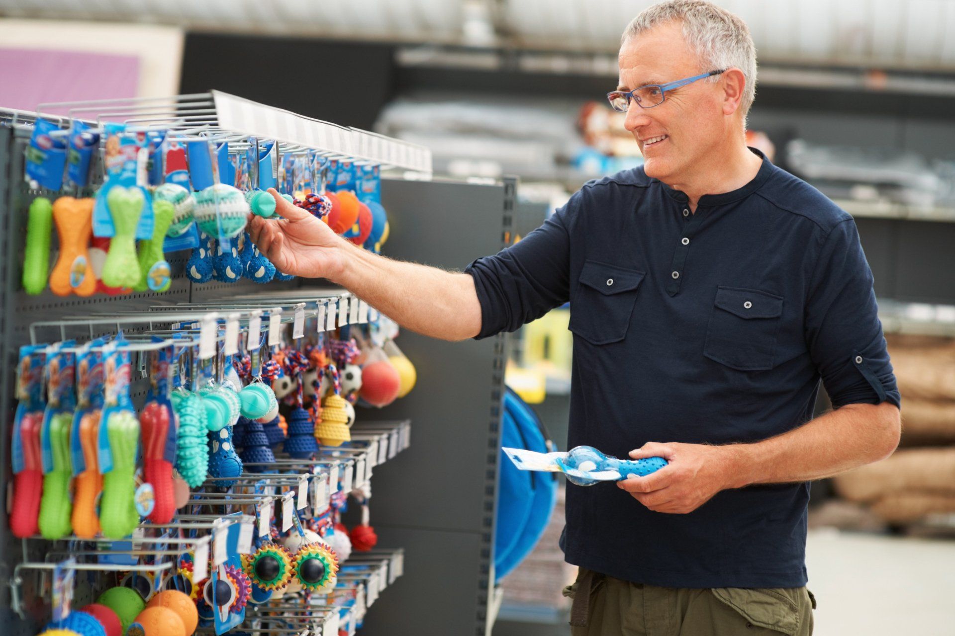 Man Checking Pet Supplies — Madison, WI — Noah's Ark Pet Center Man shopping for dog toys in a store, reaching for a blue toy.