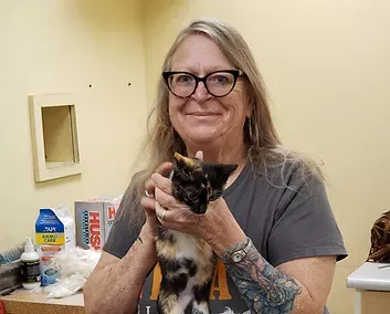 Karla — Madison, WI — Noah's Ark Pet Center Woman with glasses holds a calico cat indoors. She smiles, and has a tattoo on her arm.
