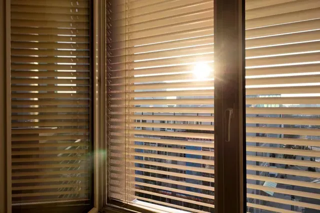Sunlight shining through closed window blinds, casting warm light indoors