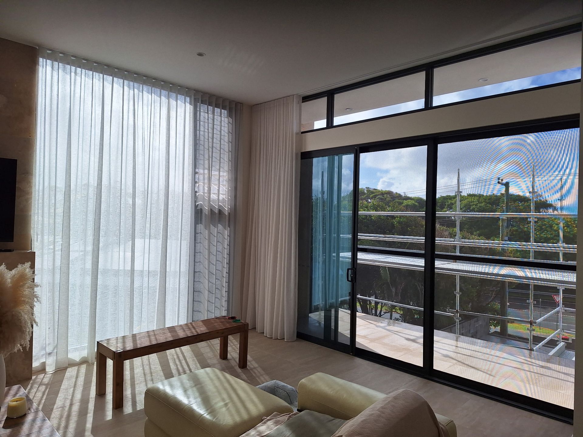 Modern living room with large sliding glass doors, sheer curtains, and a balcony view of greenery.