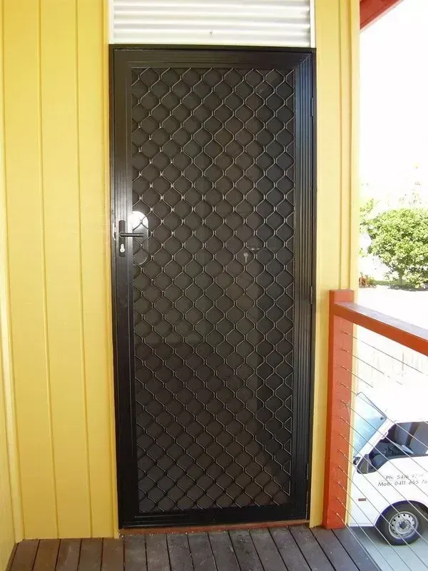 Black Security Screen Door in Yellow Siding Entryway With a Small Cart on the Porch — Another Blind Man in Tewantin, QLD