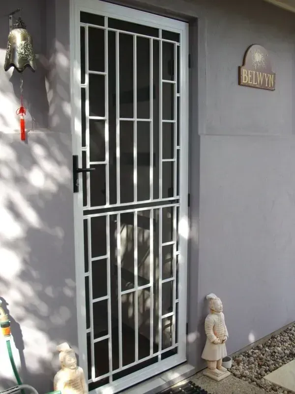 White Security Door on a Grey House Exterior With a Small Statue — Another Blind Man in Tewantin, QLD