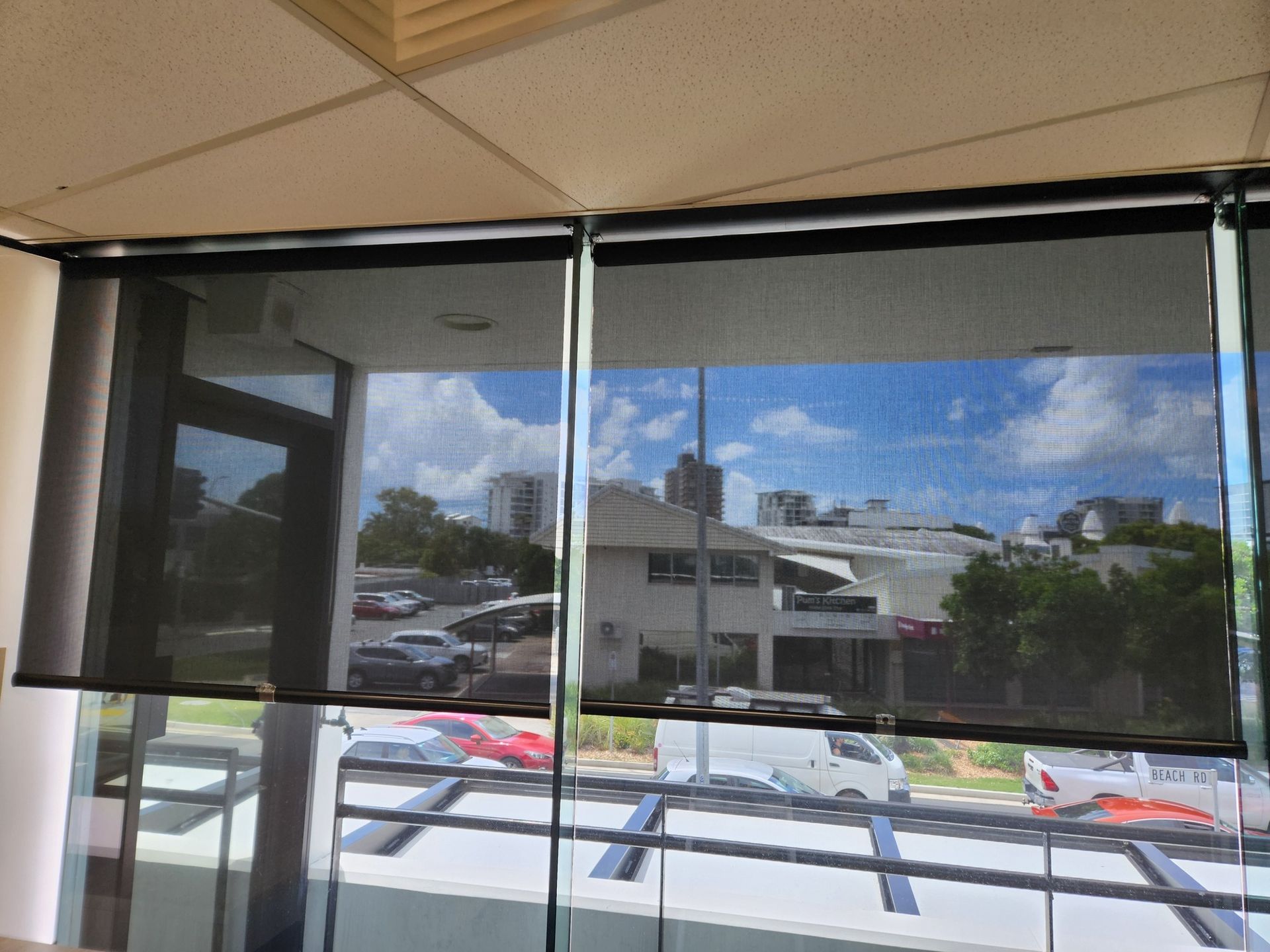 Black mesh window shades over a sunny patio view with a house and parked cars outside — Another Blind Man in Tewantin, QLD
