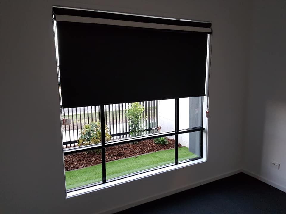 Empty room with a window and black roller blind, showing a fenced garden outside — Another Blind Man in Tewantin, QLD