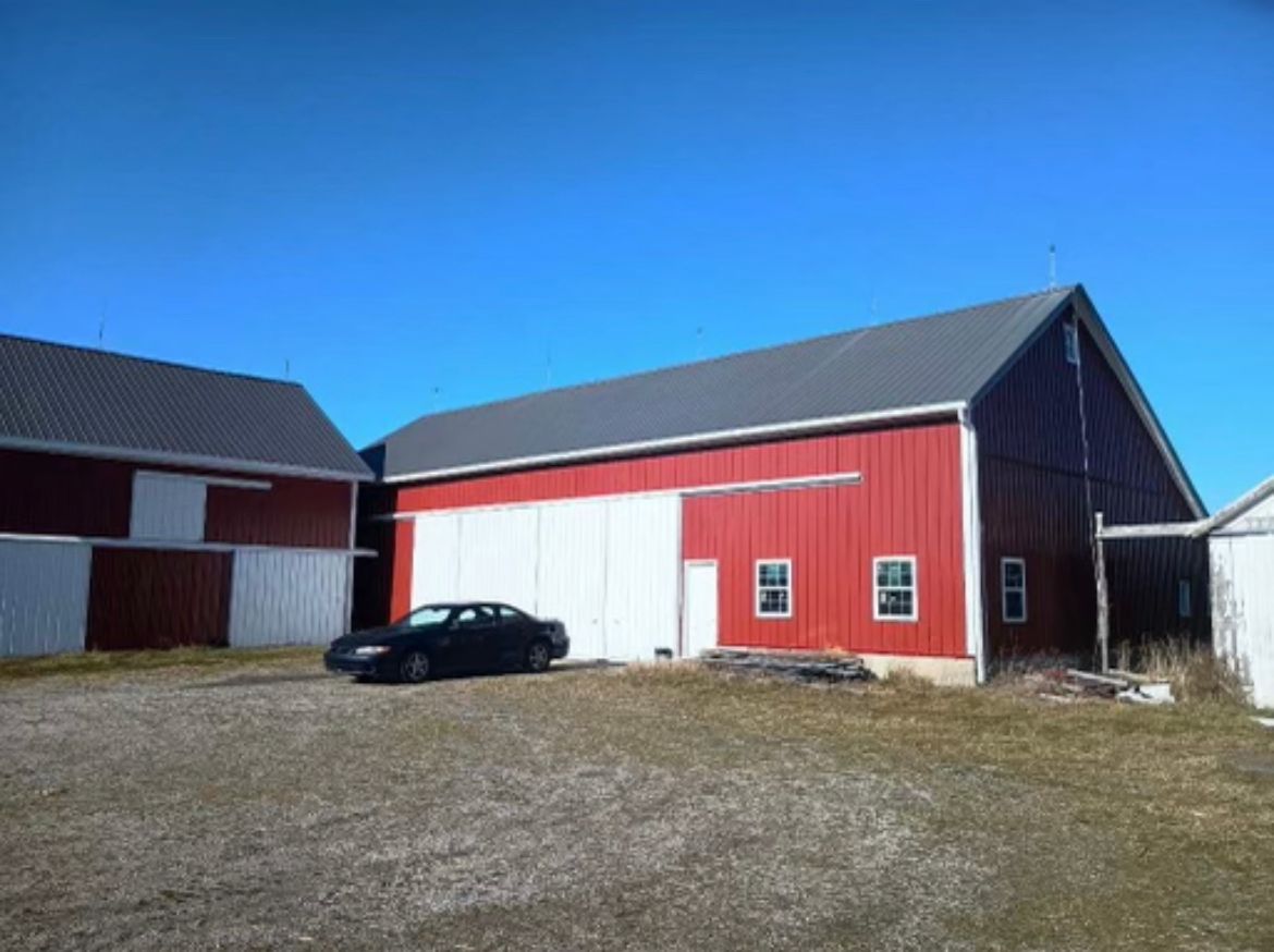 Red barns with white doors, gravel driveway, and clear blue sky, showcasing ideas on how to build a ranch in a rural setting.