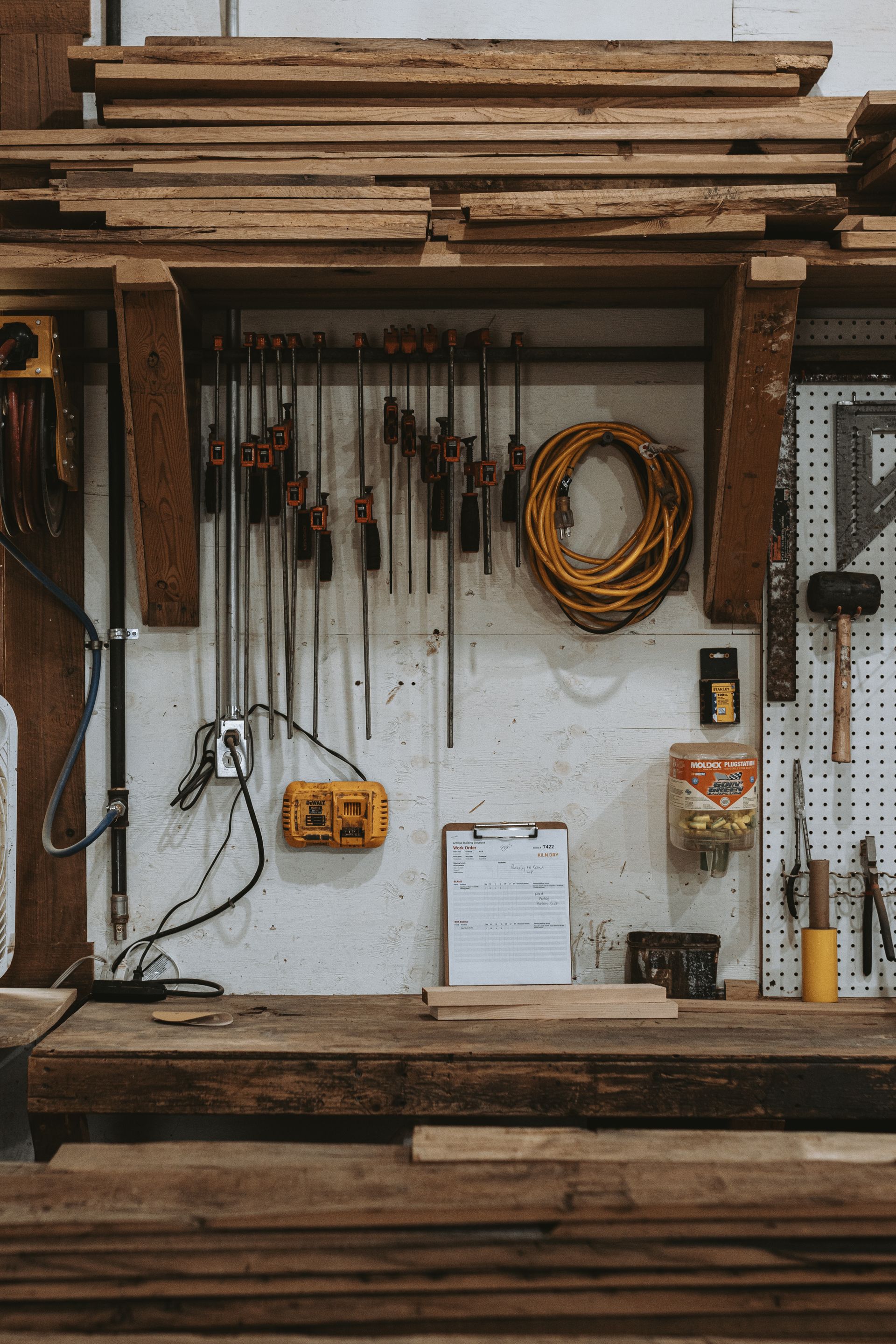 Timber frame tools beneath a reclaimed beam rack in a Pennsylvania restoration workshop.
