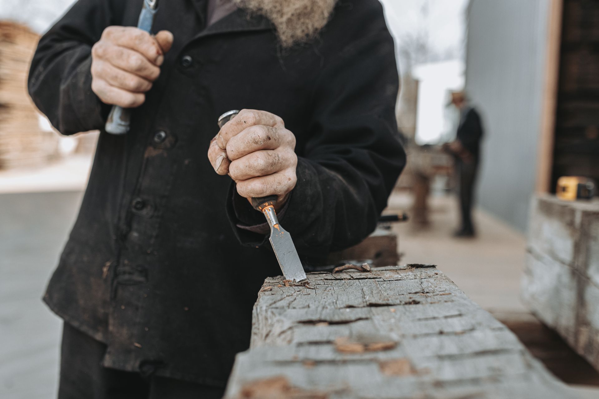A man is hand hewing a reclaimed piece of vintage barn wood. 