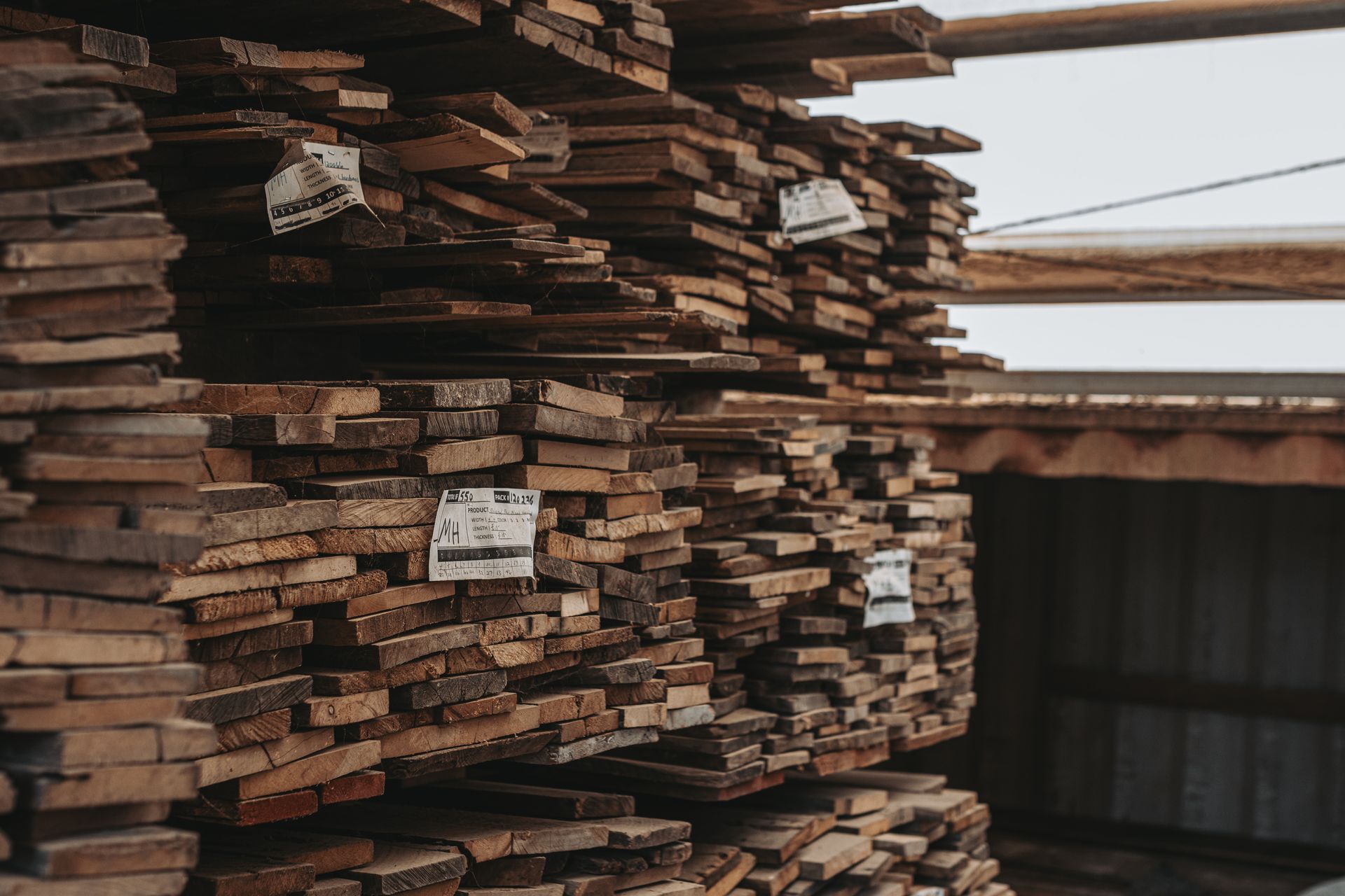 Stacks of aged wooden planks with inventory tags in a storage shed for antique timber salvage and reuse.