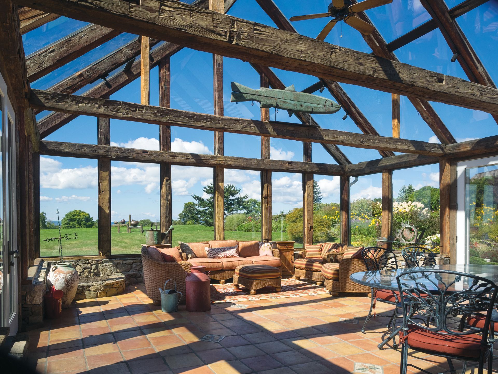 Sunroom with rustic timber beams, glass ceiling, and countryside views, showcasing a barn converted to house living space.