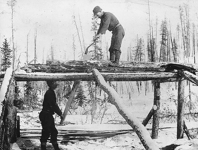 Bay & Bent USA men construct a log structure in a snowy forest using ancient woodworking techniques