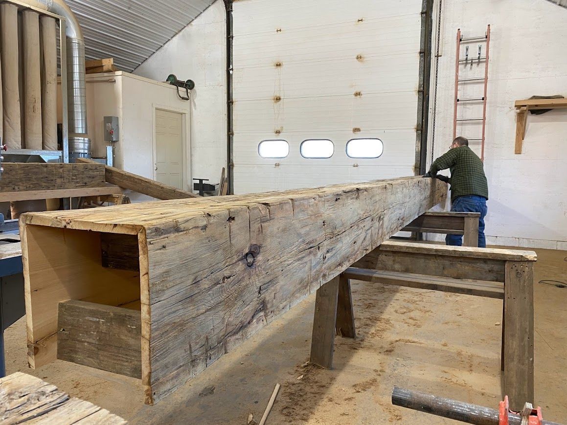 Woodworker crafting with reclaimed hand-hewn beams in workshop.