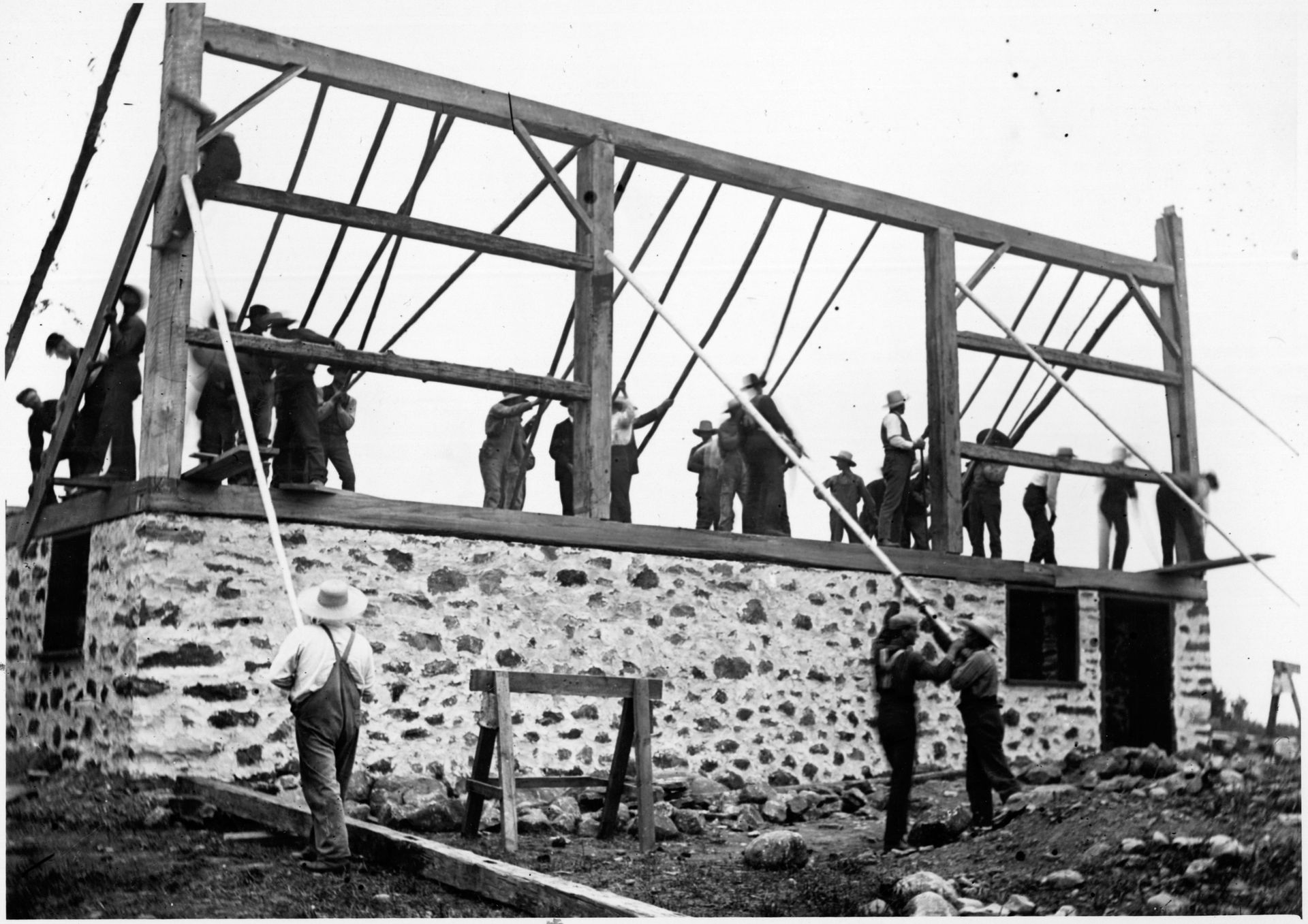 Workers raise a timber frame on a stone foundation, showcasing Pre-Civil War timber craftsmanship.