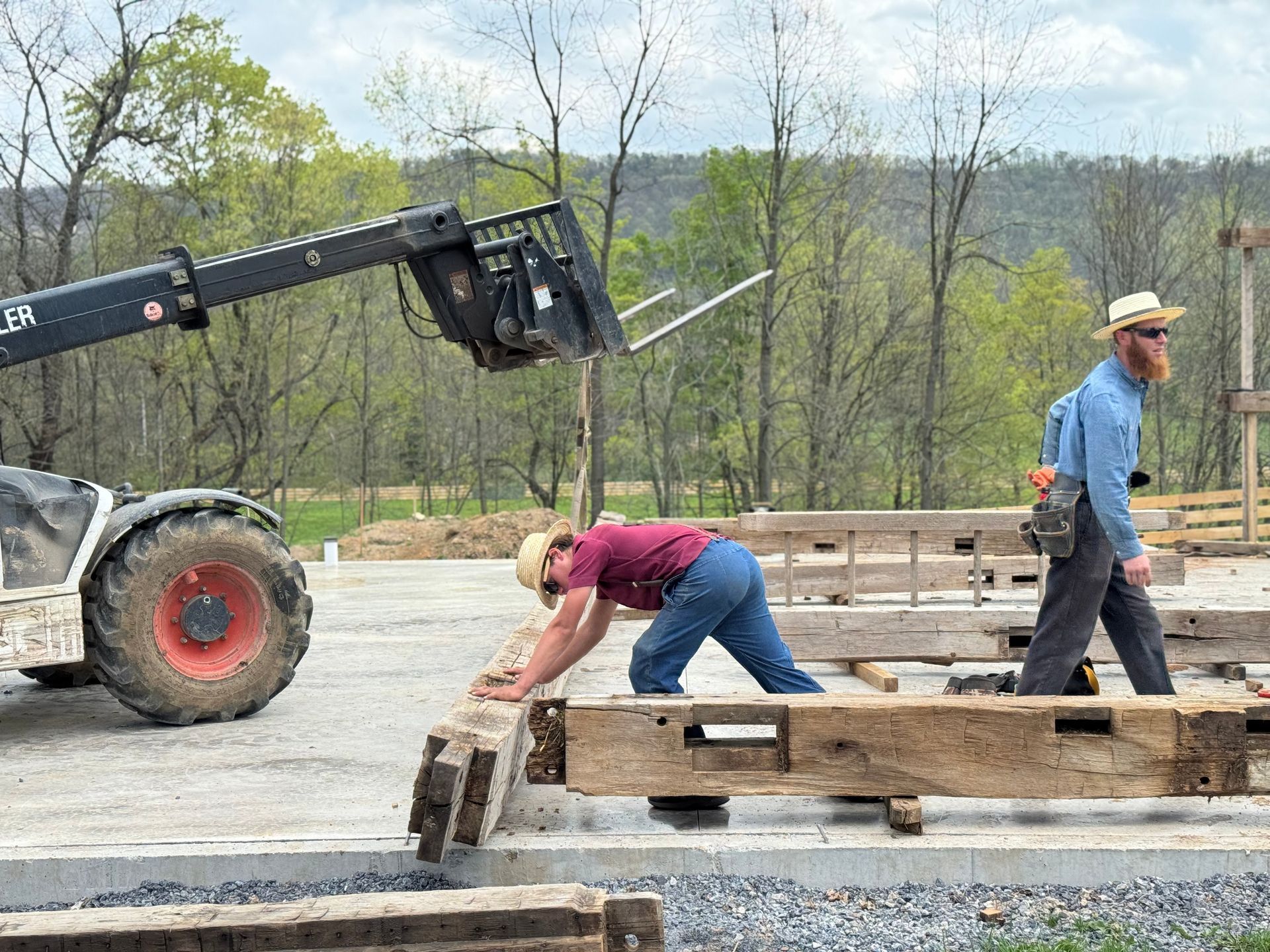 Crew using a forklift to place timber beams at a metal building homes construction site.